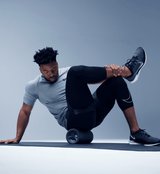 Man seated on a mat rolling his lower leg over a vibration roller